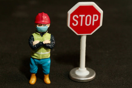 miniature construction worker wearing face mask and stop sign on black backgroundの写真素材