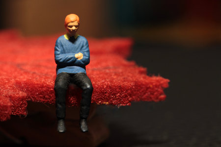Miniature people: Sad man sitting on a red cloth. Selective focus.の写真素材