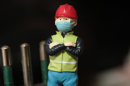 Miniature people construction worker wearing face mask to protect from COVID-19 or Coronavirus