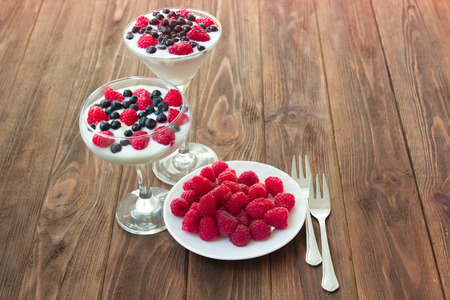 yogurt dessert with raspberries and blueberries in glasses on the wooden tableの写真素材