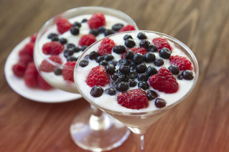yogurt dessert with raspberries and blueberries in glasses on the wooden tableの写真素材