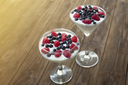 yogurt dessert with raspberries and blueberries in glasses on the wooden tableの写真素材