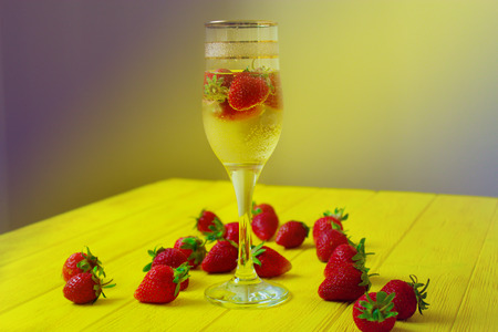 glass of champagne with strawberries on the bright yellow wooden tableの写真素材