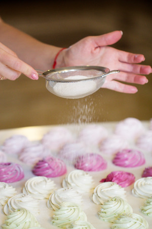 Woman's hands sprinkling with icing sugar a zephyr  using sieve. Confectioner sprinkles powdered sugar on marshmallowの写真素材