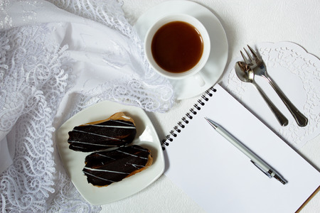 Eclairs or profiterole with chocolate, cup of coffe and notebook. Top view of notebook, coffee,...
