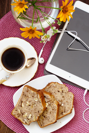 Homemade Banana cake with walnuts. breakfast with notebook and smart phone on wooden table.top viewHomemade banana bread.の写真素材