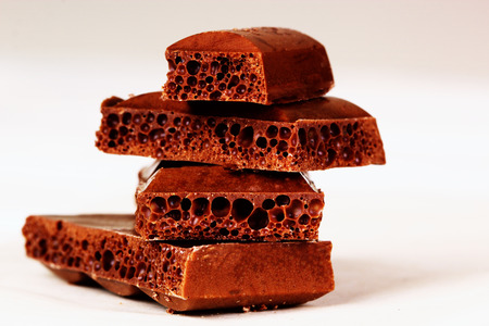 Porous black chocolate on a white background in macro. Pieces of porous chocolate on a white...