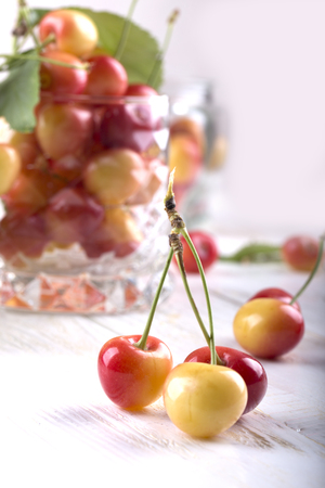Red and yellow Rainier cherries. Fresh red cherries in clear glass put on wooden tableの写真素材