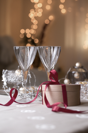 glasses of wine/ champagne glasses on the background of Christmas decorations. glasses of wine/ champagne glasses with Christmas gift box in craft paper with red ribbon.の写真素材