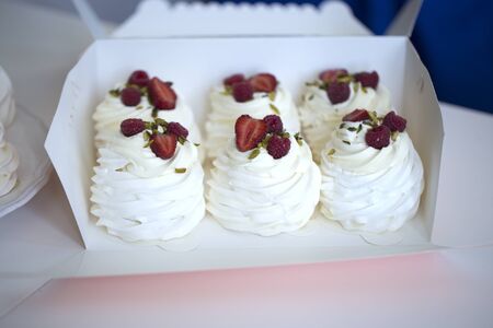 Pavlova cakes with cream and fresh summer berries. Pavlova cakes in a box. Close up view of a box full of mini meringue Pavlovas nests with cream, red fruitsの写真素材