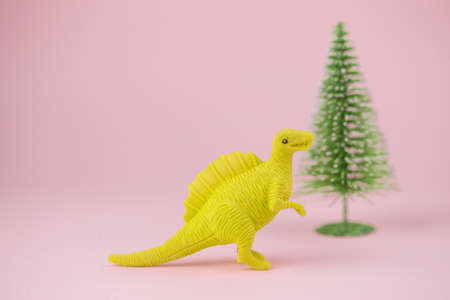 toy dinosaur with christmas tree on background. festive minimal greeting card with cute dinosaur and christmas tree on a pink backgroundの写真素材