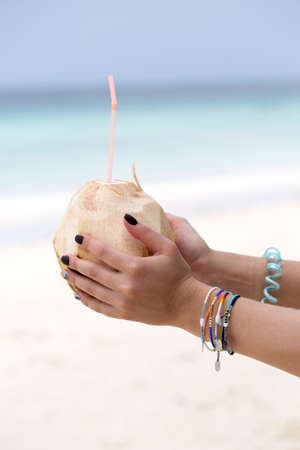 Female hands with a coconut on the beach. Female hands with delicious refreshing coconut cocktail against beautiful seaの写真素材