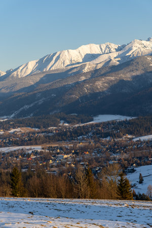 Stunning winter landscape of Zakopane, Poland, featuring the snow-covered Tatra Mountains at sunset. The picturesque alpine town, surrounded by forests and peaks, offers breathtaking views and is a popular tourist destination for skiing, hiking, and nature lovers. Captured on a clear, sunny day, this high-resolution image showcases the beauty of the Polish Alps in winter.の写真素材