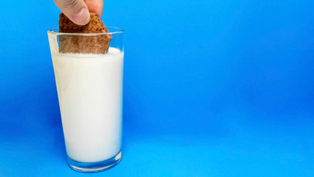 Breakfast concept. Hand dipping sandwich biscuits cookie filling with chocolate cream an to a glass with milk on blue backgroundの写真素材