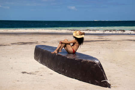sexy woman sunbathing in a bikini on top of a boat on a caribbean sea beach while watching the ocean horizon and enjoying the sea breeze and the radiant rays of the sun that create an ideal atmosphere for vacation and relaxation.の写真素材