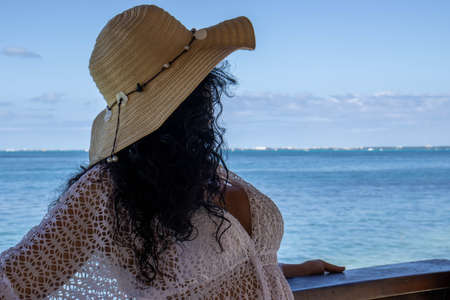 Beautiful woman relaxing and enjoying an orange sunset on a pier over the turquoise Caribbean sea.の写真素材