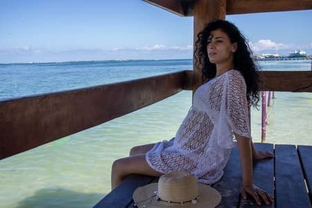 Sexy woman sitting and resting happily on a dock while enjoying the turquoise color of the sea and the Caribbean sun, this is an ideal vacation and summer tourism spot.の写真素材