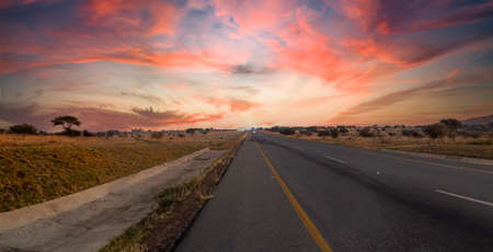 Travel on a road that runs through the middle of the African savannah of South Africa at sunset, it...