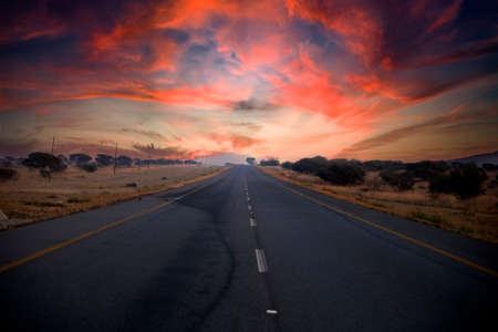 Beautiful South African road that runs through the middle of the African savannah under the typical African sun, which is characterized by beautiful colors at sunset.の写真素材