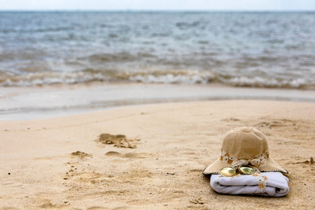 Beach cap with a towel and sunglasses on a white sandy Caribbean beach under the radiant and warm rays of the sun, ideal place for tourists to enjoy summer vacations.の写真素材