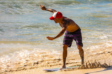 Playa del Carmen, Mexico - March 10, 2023: Man practicing skimboarding which is a modality that is practiced on the shore and that consists of surfing the shore waves with a smaller and thinner board.のeditorial素材