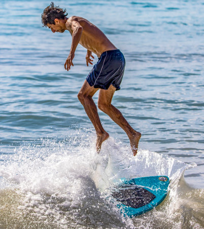 Playa del Carmen, Mexico - March 12, 2023: Man surfing and jumping over the waves of the Caribbean Sea with his small skimboard, this is an ideal water sport.のeditorial素材