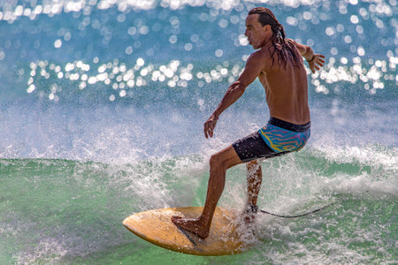 Playa del Carmen, Mexico - March 12, 2023: Athletic man surfing the waves of the Caribbean Sea with his board and enormous agility is an ideal water sport that concentrates strength and balance.のeditorial素材