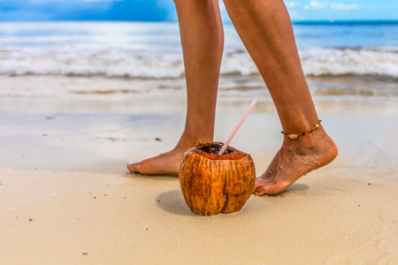 Feet of a tourist walking next to a coconut on a white and golden sand beach with the Mexican Caribbean Sea in the background, this is a relaxing and wellness scenery and ideal for vacations.の写真素材