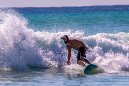 Playa del Carmen, Mexico - May 2, 2023: Person practicing surfing which is a water sport that navigates over the wings with a surfboard. Man standing with balance on a surfboard. Water sports concept.のeditorial素材