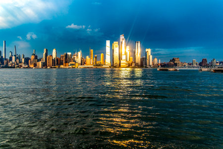 Skyline of New York and the Big Apple seen from a viewpoint on the Hudson River, under a sunset and the sun's rays reflecting on the buildings.の写真素材