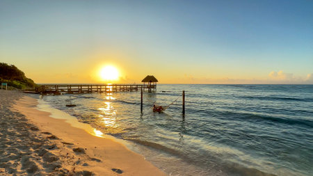 Woman lying in a hammock being swayed by the waves over the Caribbean Sea under a beautiful orange sunrise, this is a relaxing experience and a wonderful and healthy lifestyle.の写真素材