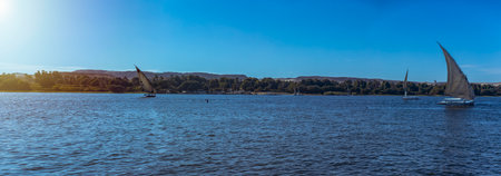 Aswan, Egypt; January 18, 2024: Experience the striking contrast of the lush coastline and desert from a Nile River felucca in Egypt. This picturesque ride on the Nile shows the diverse landscapes.の写真素材
