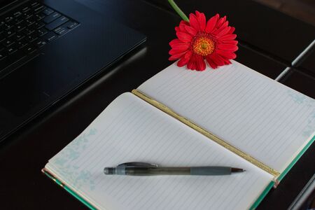 Notebook with a nice rose and laptop on wooden tableの写真素材