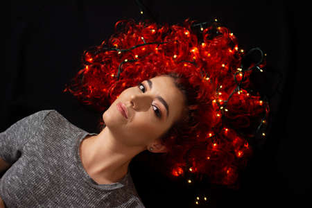 Happy woman lying on the floor of her house with Christmas lights in her hair