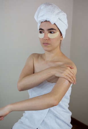 Woman with patches on her face for skin care and putting cream on her arms at homeの写真素材