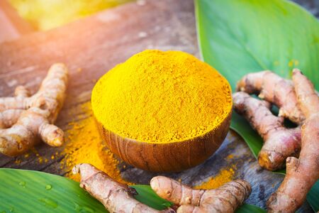 Turmeric powder and fresh turmeric in wooden bowls on old wooden table. Herbs