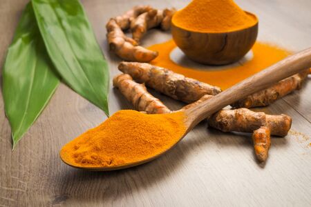 Turmeric powder in wooden spoon on old wooden table. Herbs are native to Southeast Asia.
