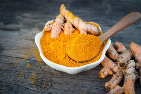 Turmeric powder and fresh turmeric in white bowls on old wooden table. herbalの写真素材