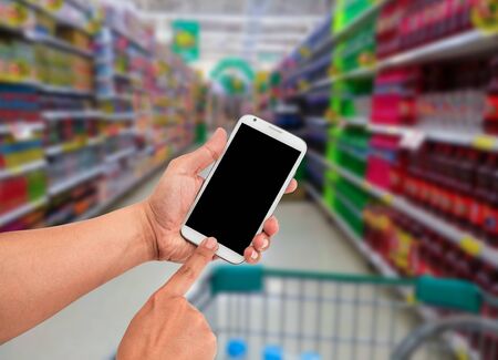 Man hand hold and touch screen smart phone, shopping center or super market background.の写真素材