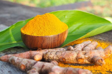 Turmeric powder and fresh turmeric with green leaf in wooden bowl on old wooden table. herbalの写真素材