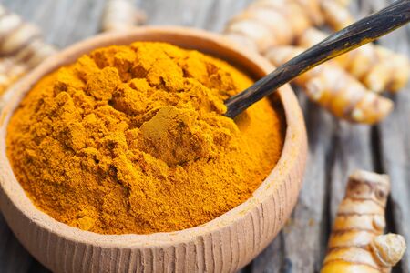 Turmeric powder in bowls and fresh turmeric on old wooden background. Herbs are native to Southeast Asia.の写真素材