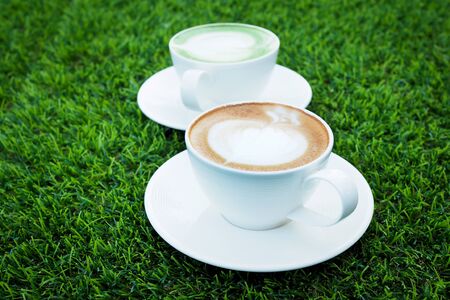 Art of Hot latte coffee and hot green tea in white cup on green grass backgroundの写真素材