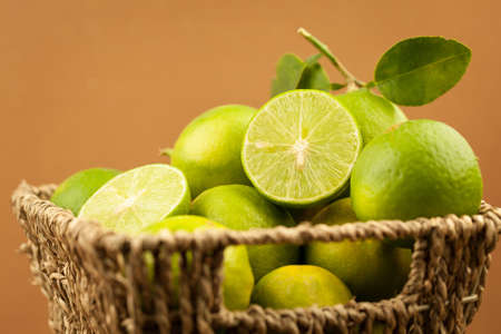 Fresh green lemon with green leaves in basket on brown background, limeの写真素材