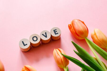 Orange tulips on pink background with cubes forming a love wordの写真素材
