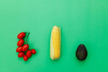 Top view of golden fresh sweetcorn, tomatoes and avocado on green background. Fresh vegetables for...