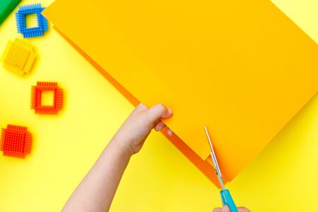 Child cutting colored orange paper with scissors  on a table for some craftworkの写真素材
