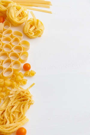 Various uncooked pasta on white wooden background. Top view. Italian pasta for restaurant with space...