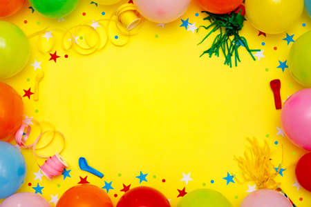 Colorful balloons and confetti on yellow table top view. Festive or party background. Flat lay style. Birthday greeting card. Carnival.の写真素材