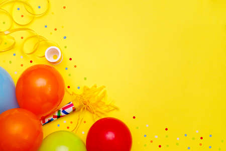 Colorful balloons and confetti on yellow table top view. Festive or party background. Flat lay style. Birthday greeting card. Carnival.の写真素材