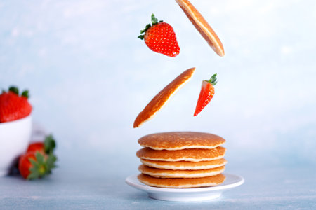 Plate with american pancakes with flying ingredients, pancakes, strawberries. Healthy food concept...